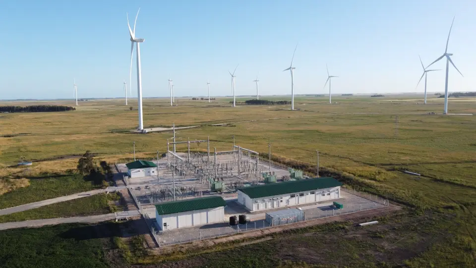 Wind farm with turbines in a field, power station in the foreground, sunny day.