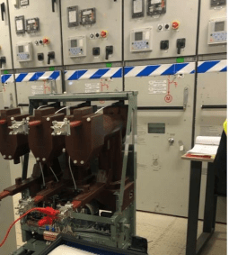 Electrical circuit breakers in front of a control panel; testing equipment attached.