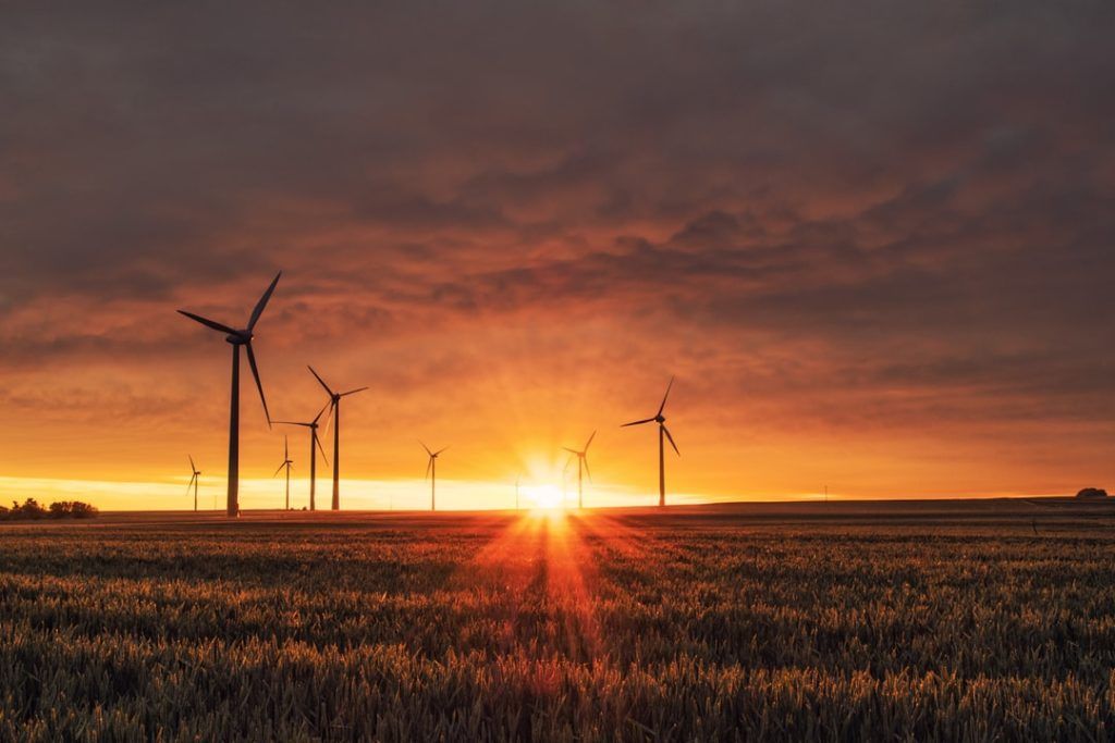 Wind turbines silhouetted against a brilliant orange sunset over a field.
