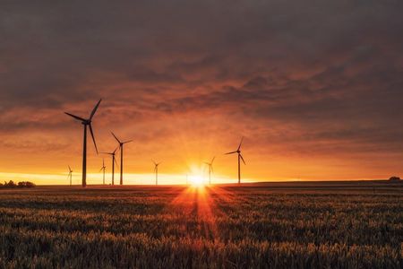 Wind turbines silhouetted against a vibrant orange sunset over a vast field.