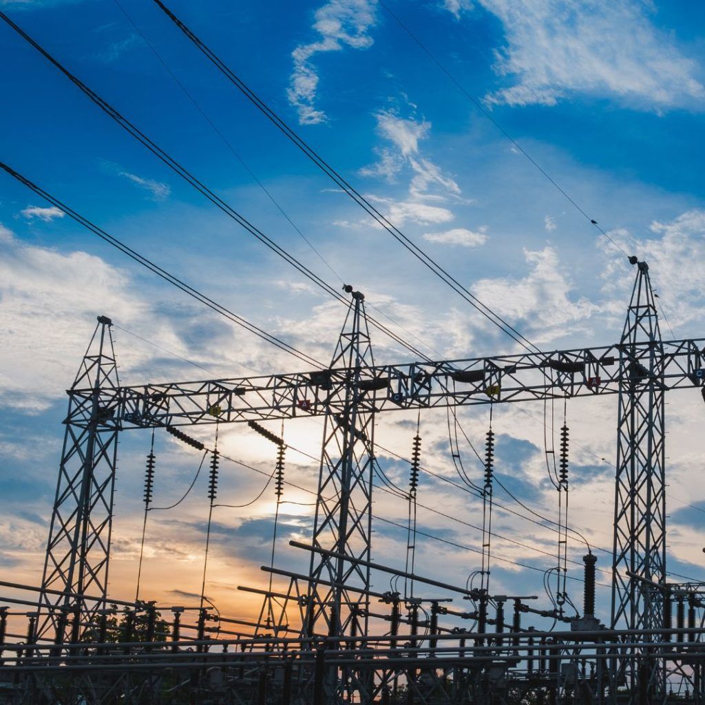 Power lines and a substation against a blue sky with clouds, sun setting in background.