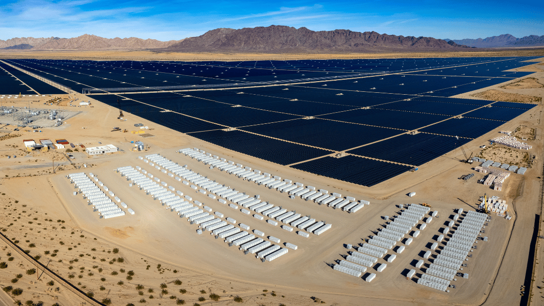 Solar panel farm in desert landscape, rows of panels with storage containers.