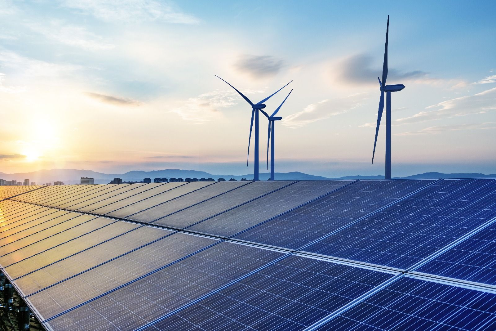 Solar panels and wind turbines generating clean energy under a blue sky at sunset.