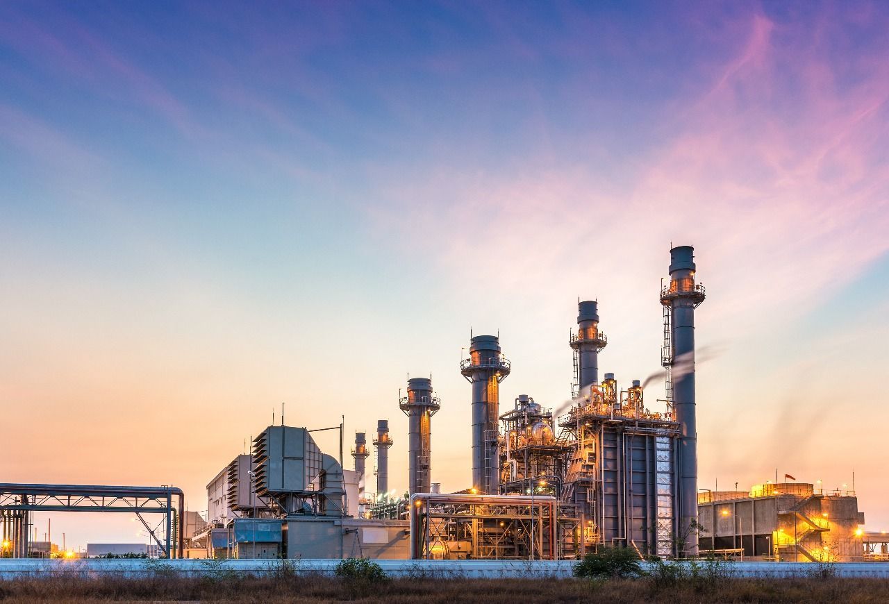 Power plant at dusk with tall smokestacks, buildings, and colorful sky.