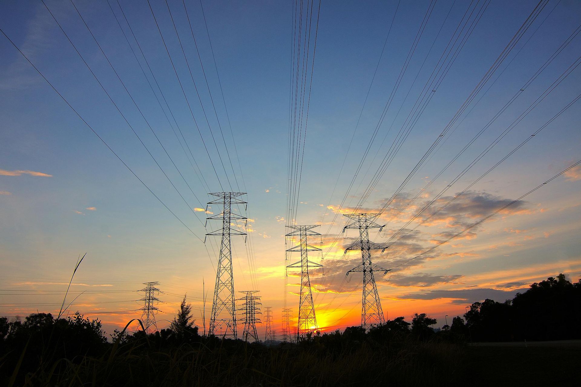 Silhouette of power lines and towers against a sunset with orange and blue sky.