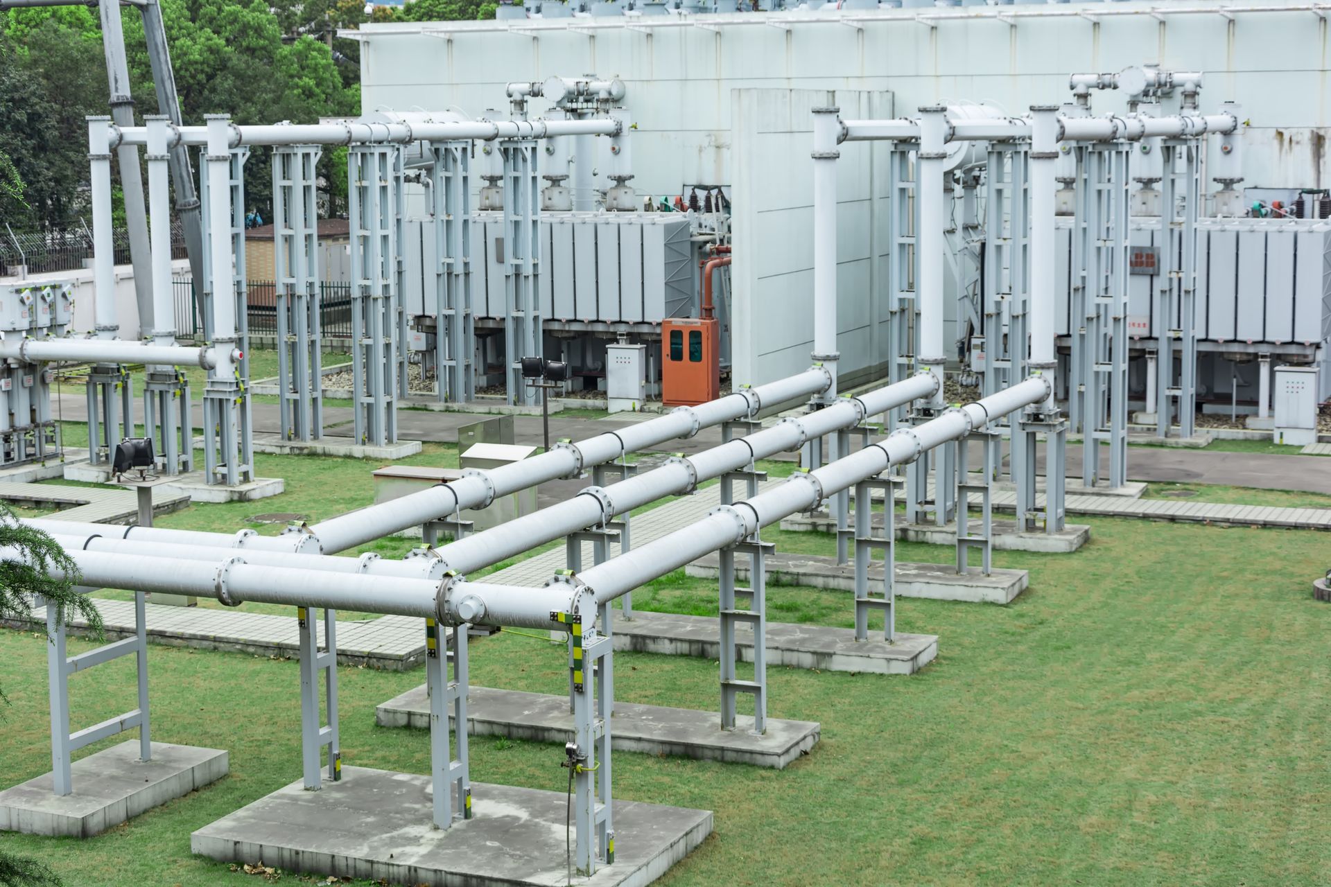 Electrical substation with transformers, pipes, and metal framework on a grassy area.