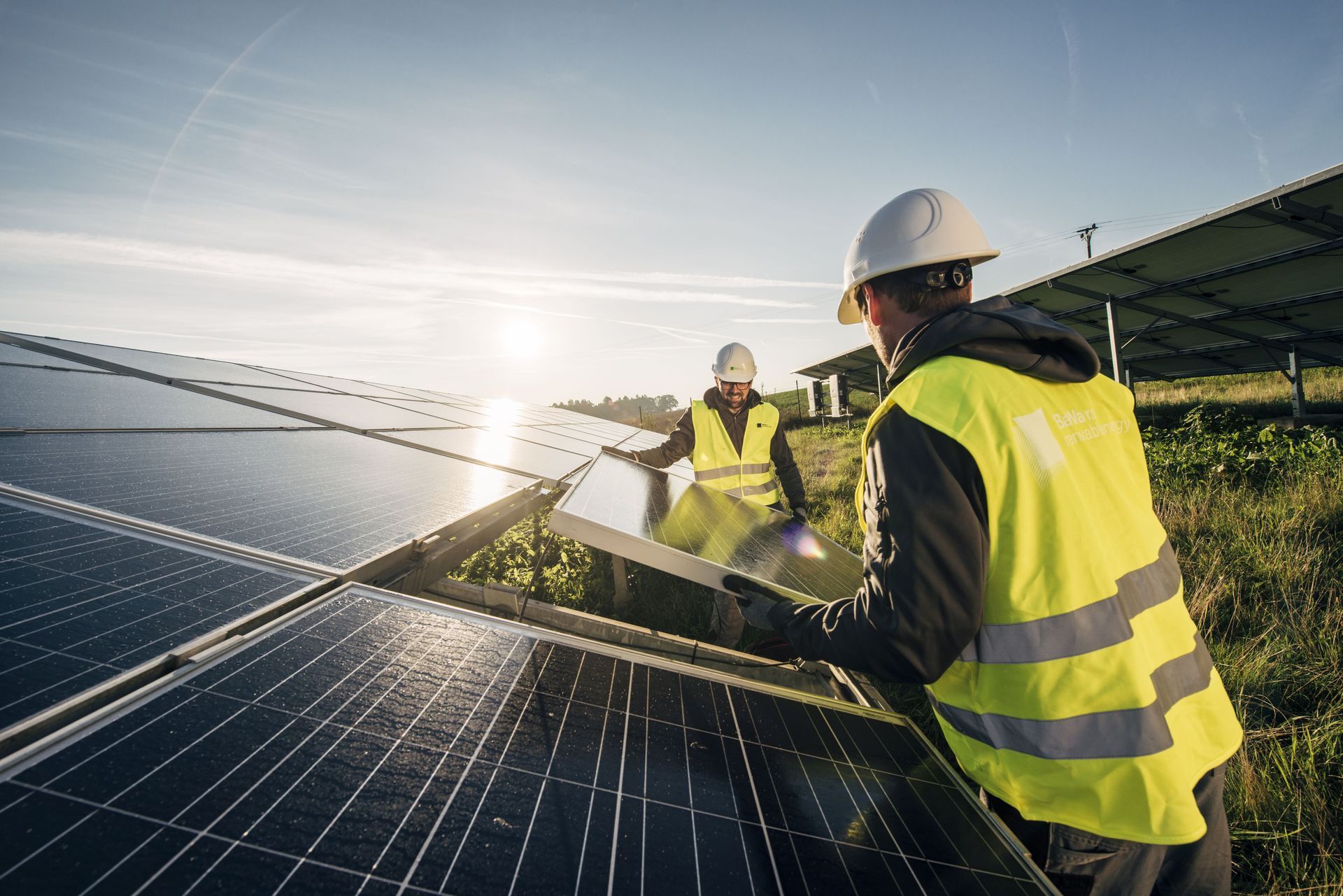 Two workers in safety vests installing solar panels outdoors on a sunny day.