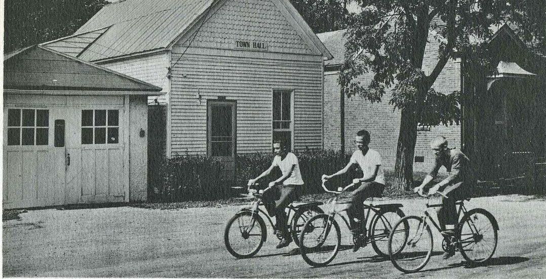 A black and white photo of people riding bicycles in front of a house