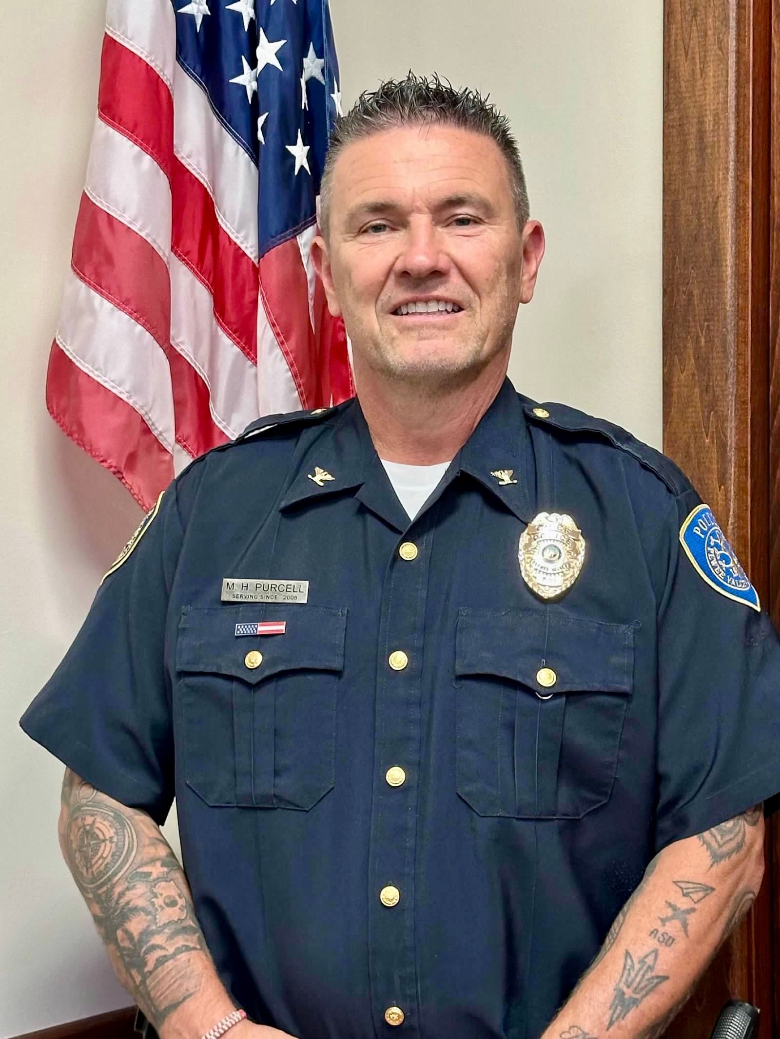 A man in a police uniform is standing in front of an american flag.
