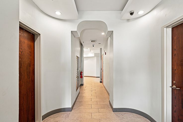 Modern hallway with white walls, curved ceiling details, tan tile floor, and wooden doors on both sides