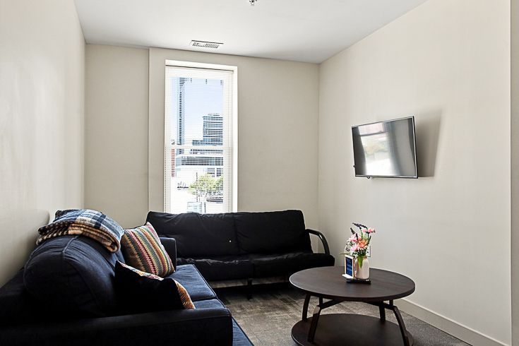 Modern living room with black sofas, wall-mounted TV, round coffee table, and a tall window with city view