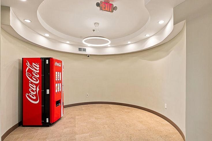 Empty beige room with a red Coca-Cola vending machine and curved recessed ceiling lights