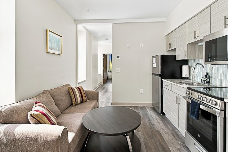 Small living room and kitchen with beige sofa, round black table, and stainless steel stove and fridge