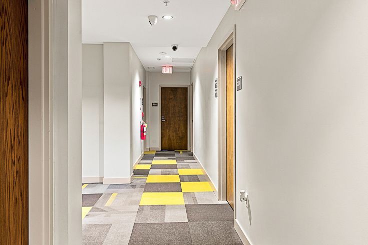 Empty hallway with gray and yellow carpet tiles, white walls, and wooden doors.