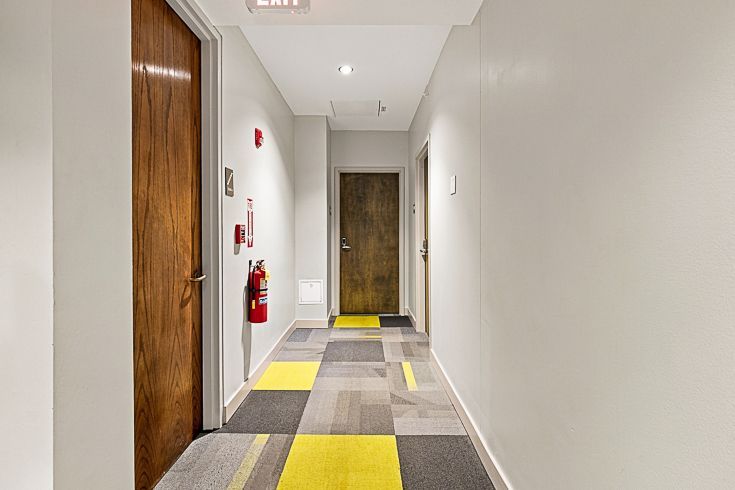 Modern hallway with white walls, wood doors, gray and yellow carpet, and a fire extinguisher on the left wall