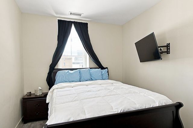 Small bedroom with a white bed, blue pillows, dark curtains, and a wall-mounted TV.