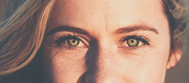 Close-up of a person's eyes, green irises, fair skin with freckles, and light-colored hair.
