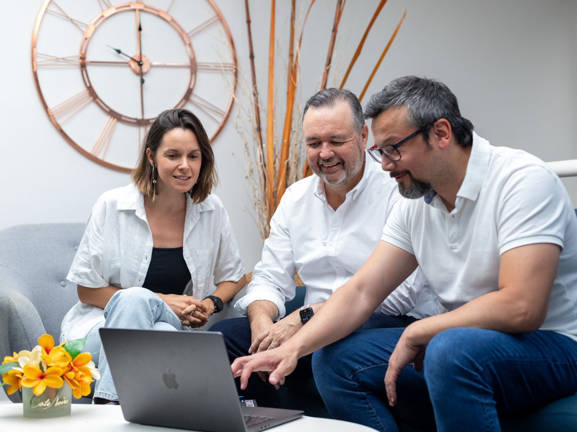 A group of people are sitting on a couch looking at a laptop computer.