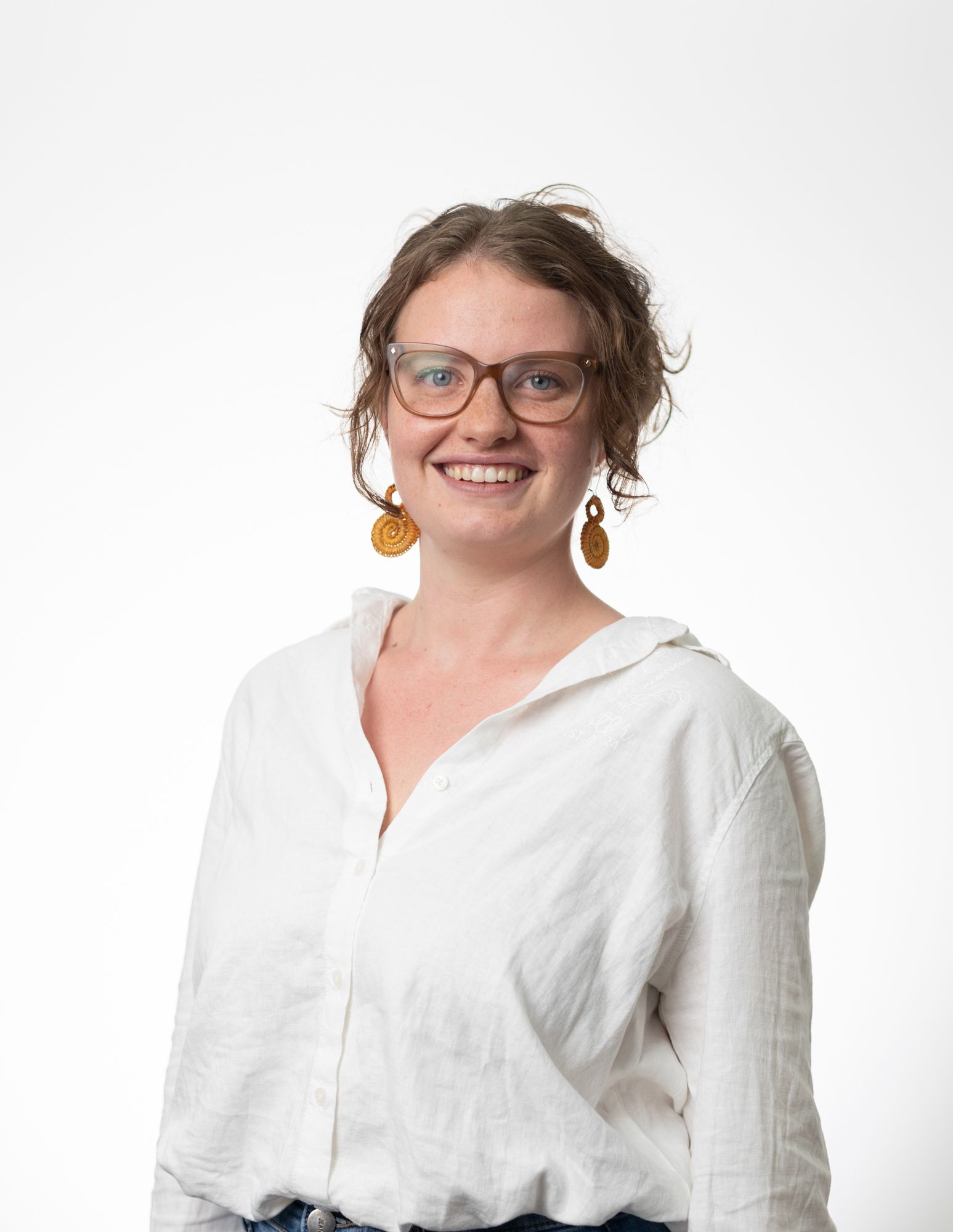 A woman wearing glasses and a white shirt is standing in front of a graffiti wall.