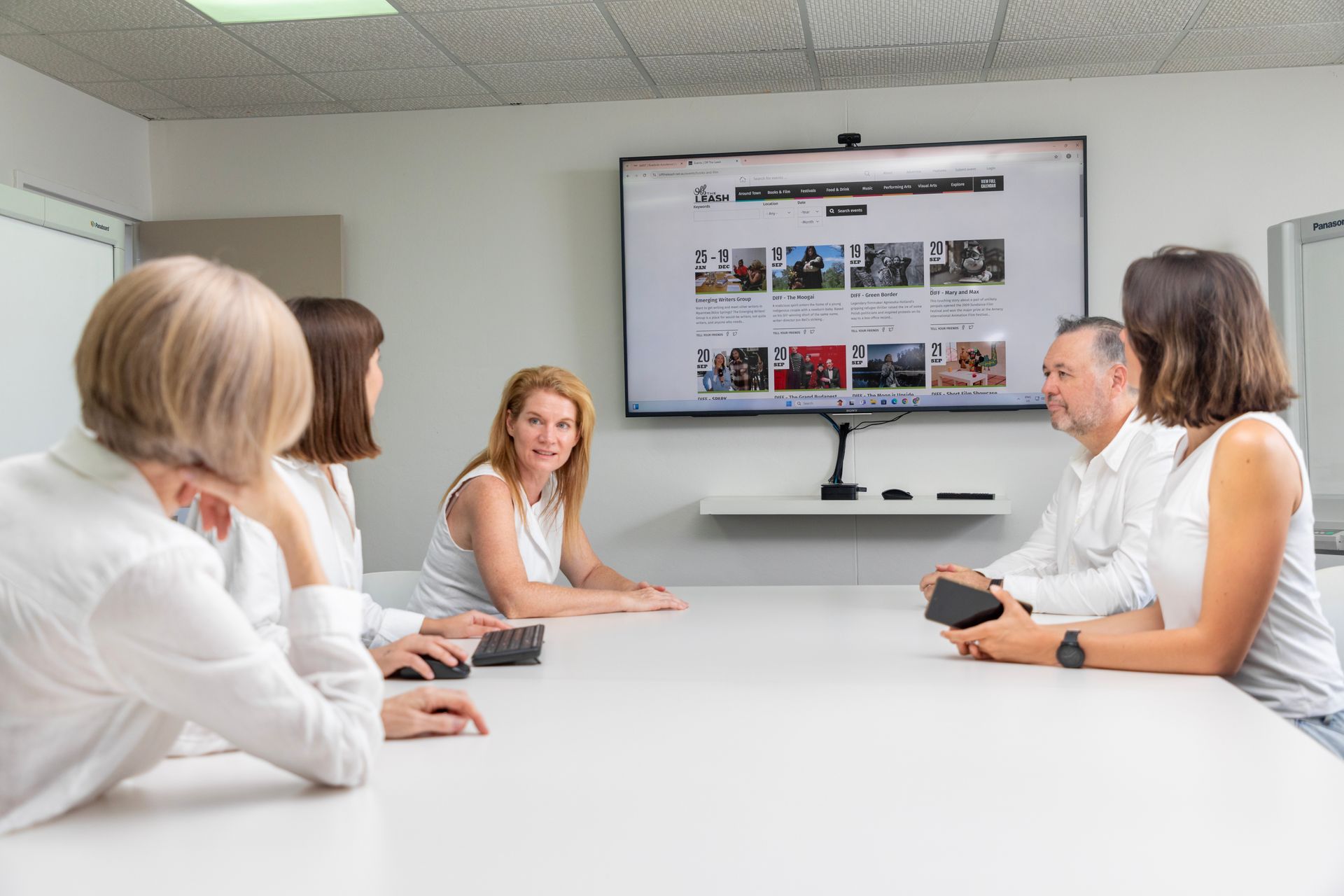 A group of people are sitting around a table in front of a large screen, having a strategy discussion.