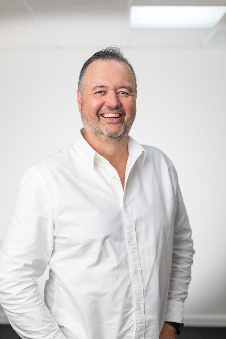 A man with a beard is wearing a white shirt and smiling.