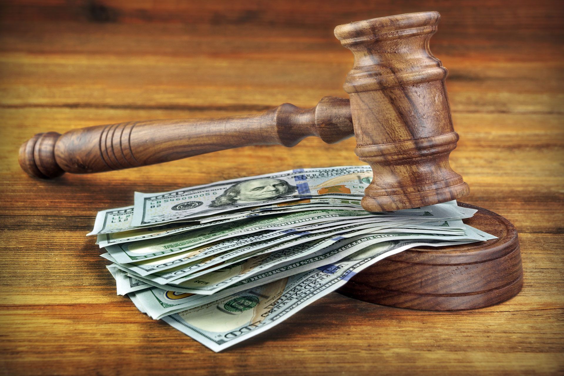A wooden judge 's gavel sitting on top of a pile of money on a wooden table