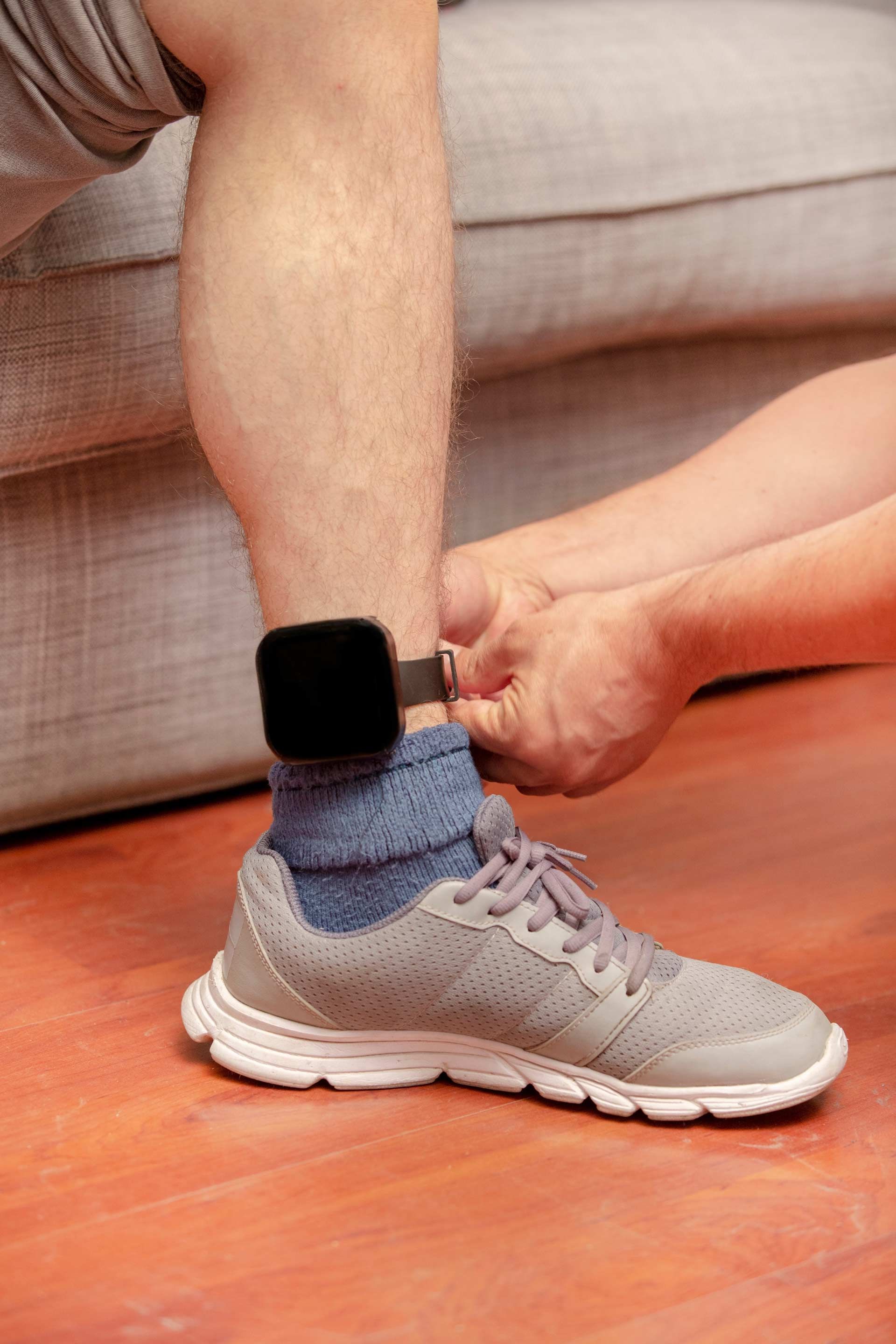 A person is tying a person 's shoe with a device on their ankle.