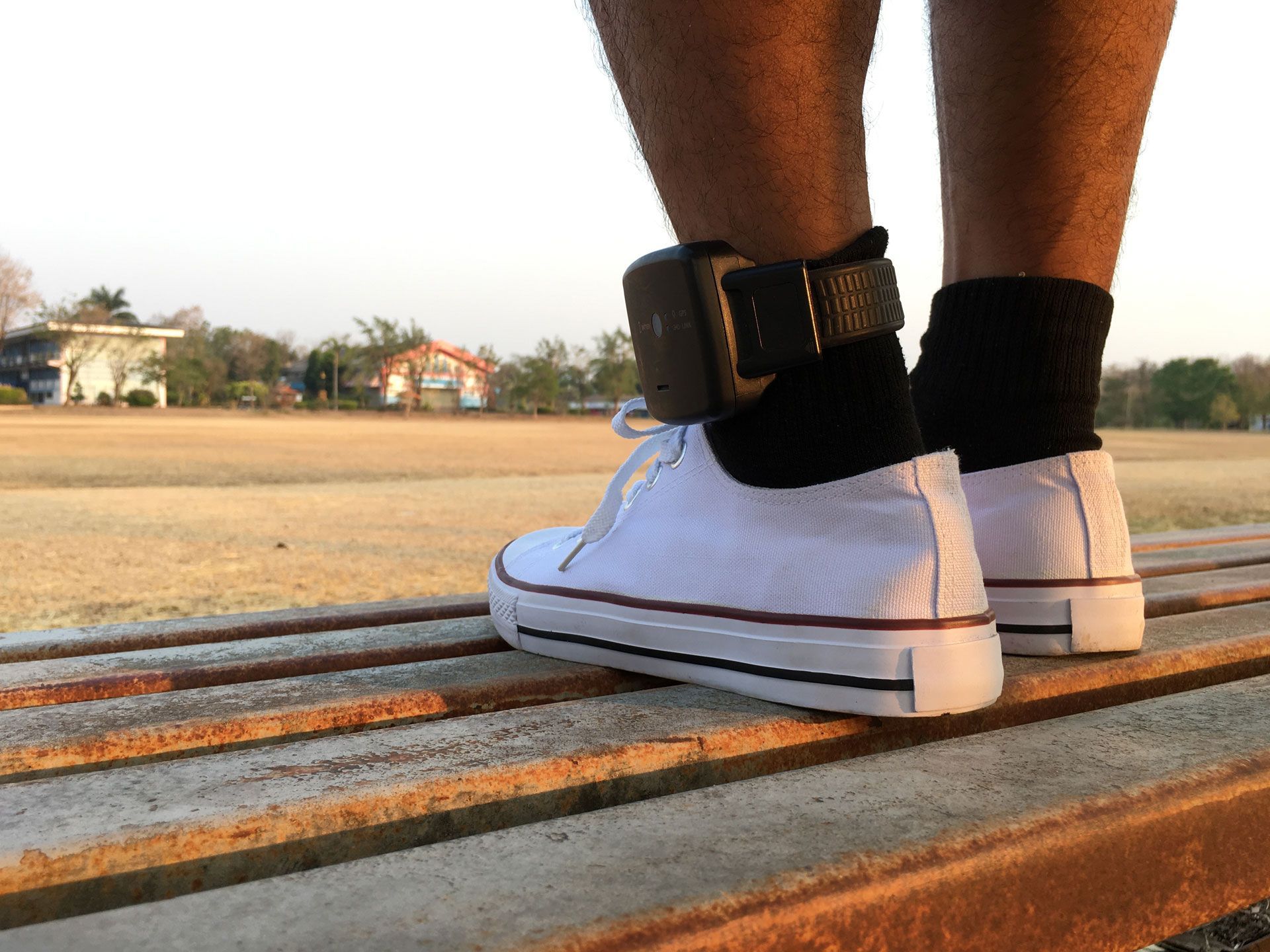 A person wearing white sneakers and black socks is standing on a bench