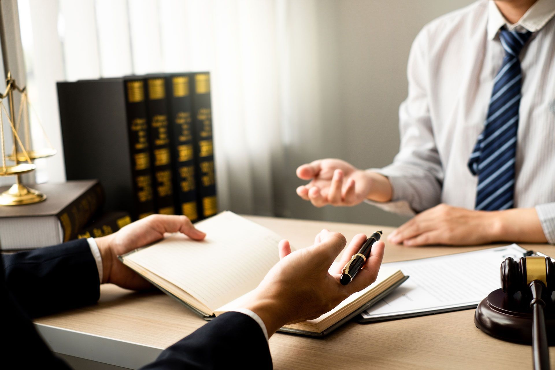 A man in a suit and tie is sitting at a desk talking to another man