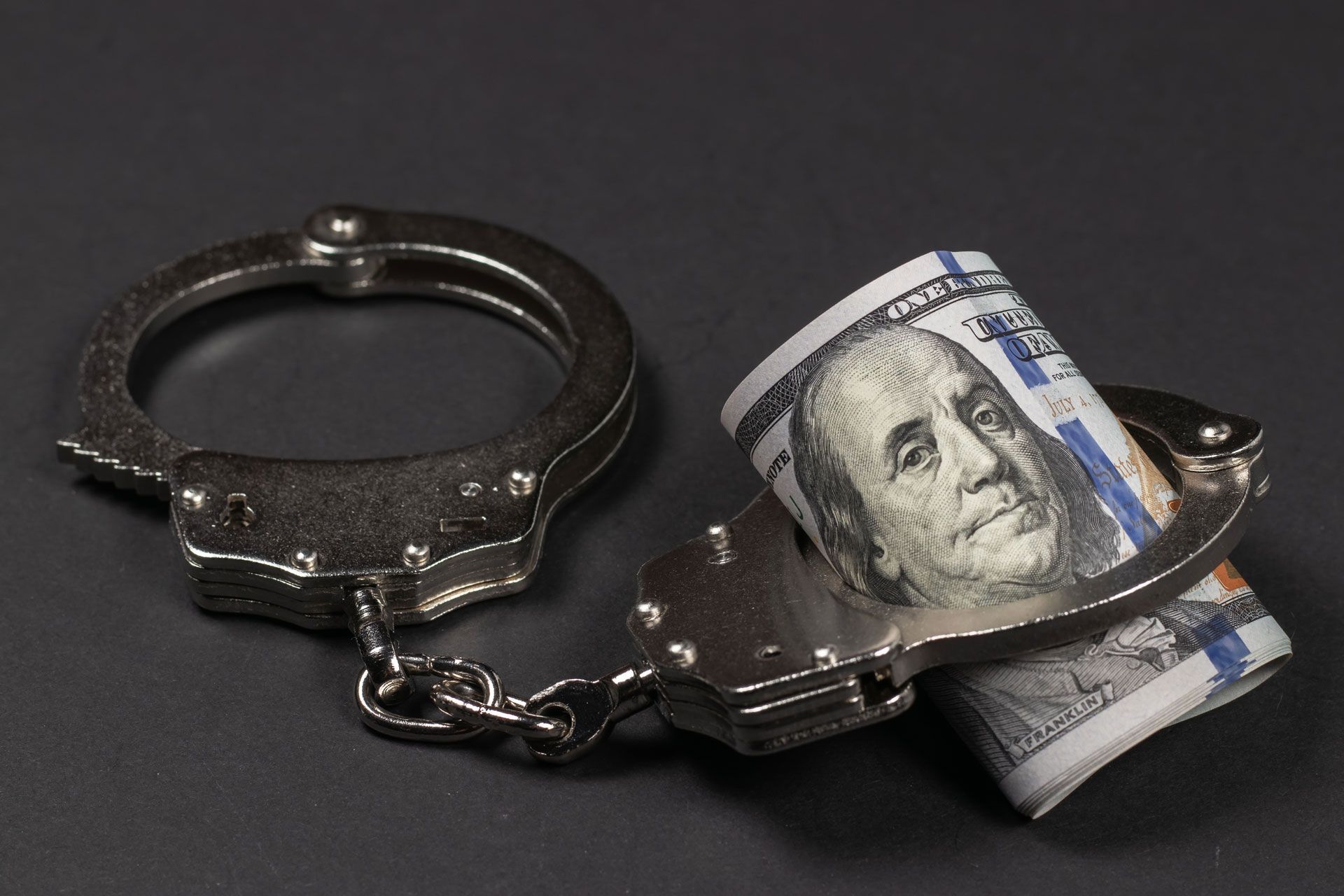 A pair of handcuffs with a 100 dollar bill in them