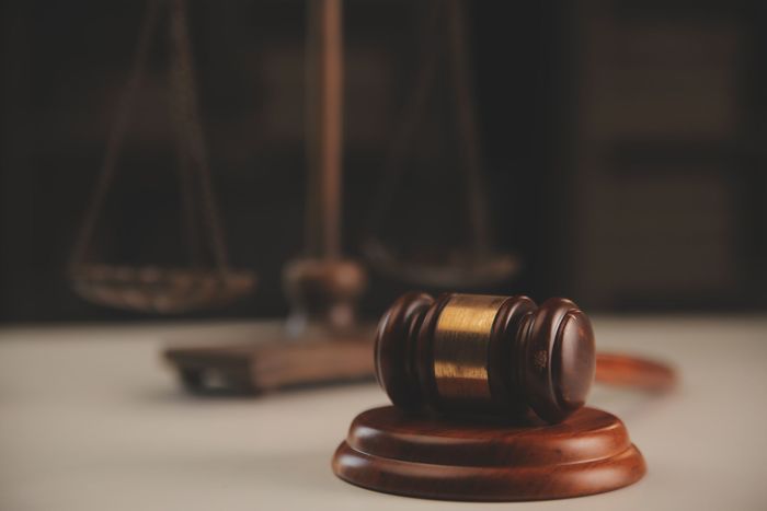 A judge 's gavel is sitting on a wooden base in front of a scale of justice