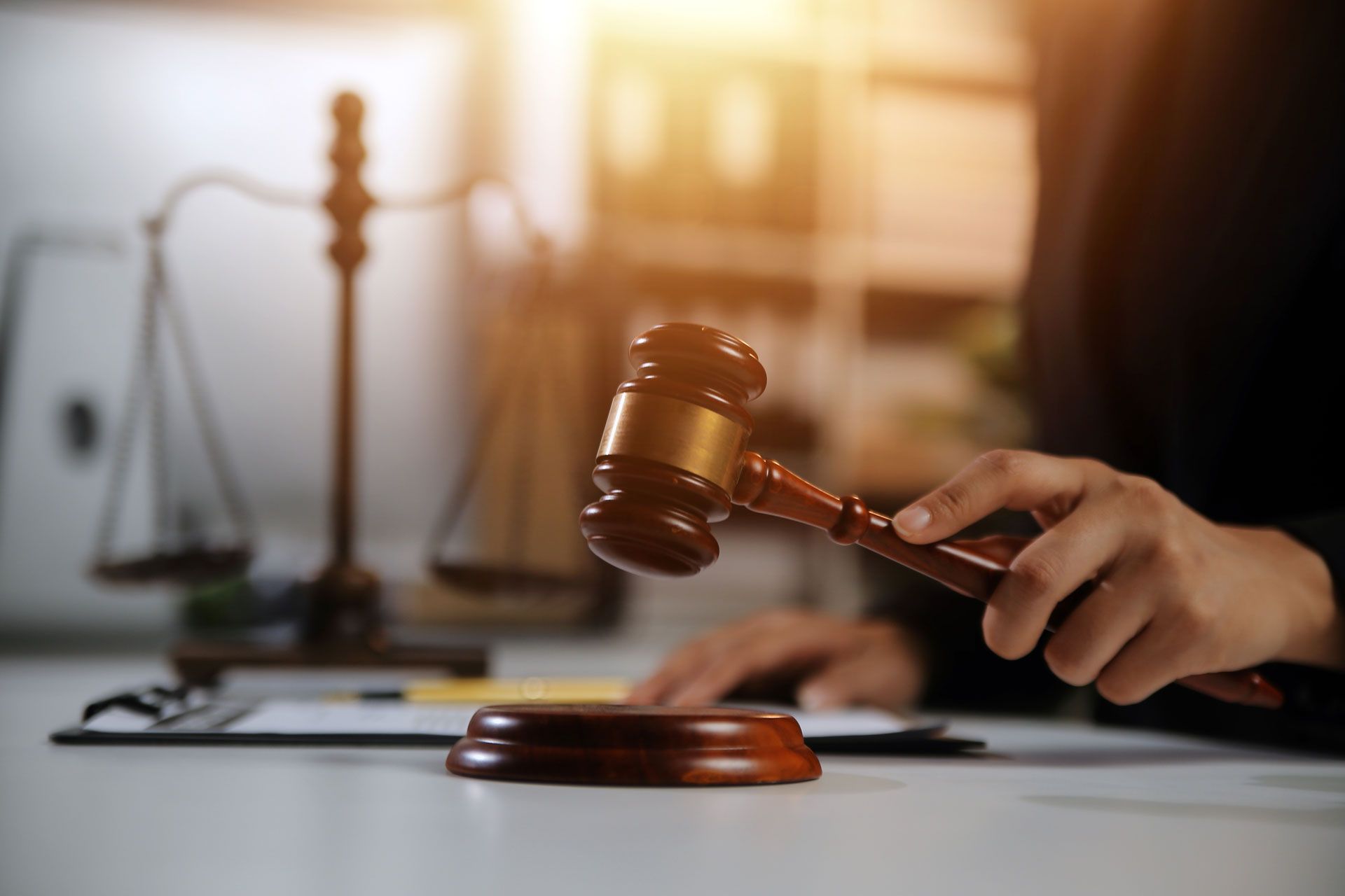 A judge is holding a wooden gavel in front of a scale of justice