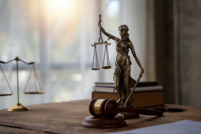 A statue of justice is sitting on a wooden table next to a gavel and scales of justice