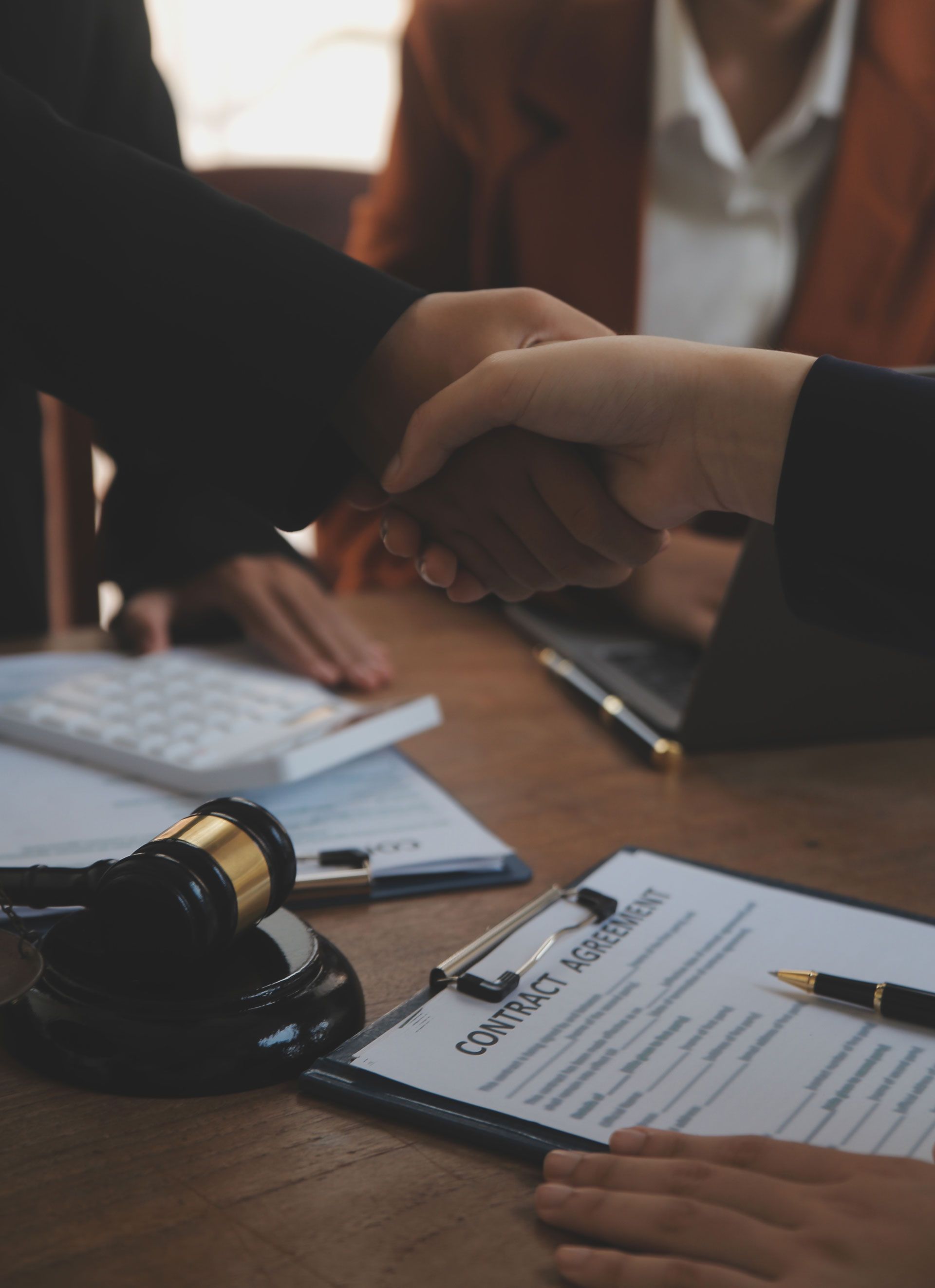 Two people shaking hands over a clipboard with a judge 's gavel in the background