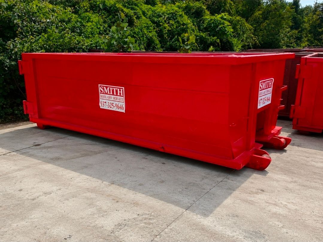A large green dumpster is parked on a brick driveway in front of a building.