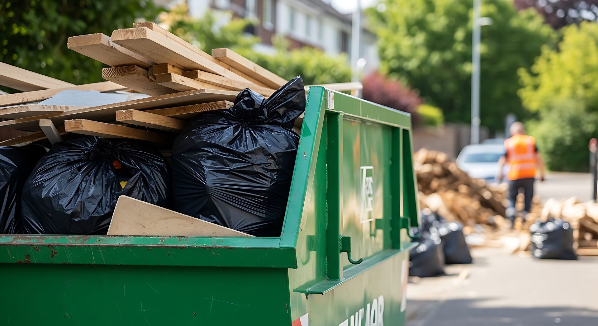Green dumpster filled with black trash bags and cardboard on a street.