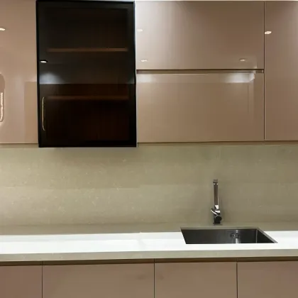 Cuisine moderne avec placards rose clair, placard haut en verre foncé, évier en acier inoxydable.