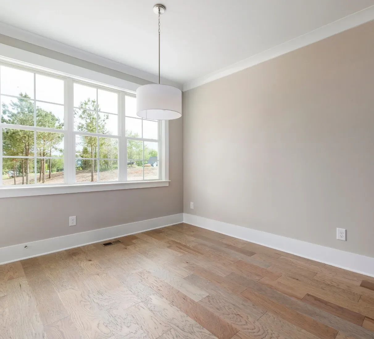 Pièce vide avec parquet clair, grandes fenêtres et murs aux tons neutres. Un lustre moderne est suspendu au plafond.