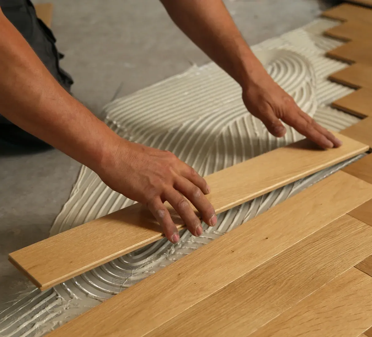 Des mains posent des lames de parquet et appliquent de la colle sur le support.