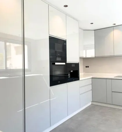 Cuisine moderne avec placards blancs et gris brillants, électroménager noir intégré et sol gris.