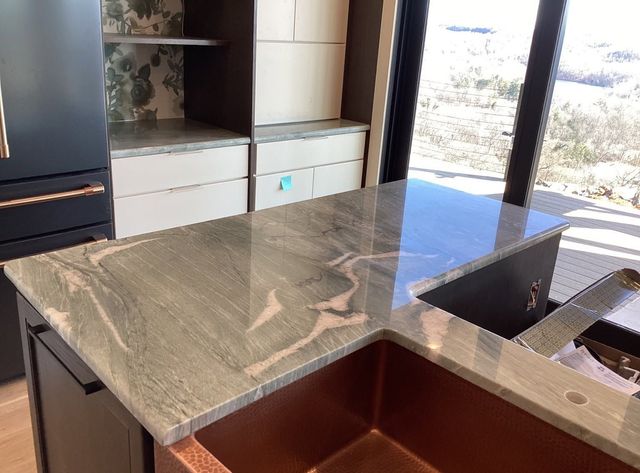 Modern kitchen island with gray marble countertop and dark wood cabinets by a window