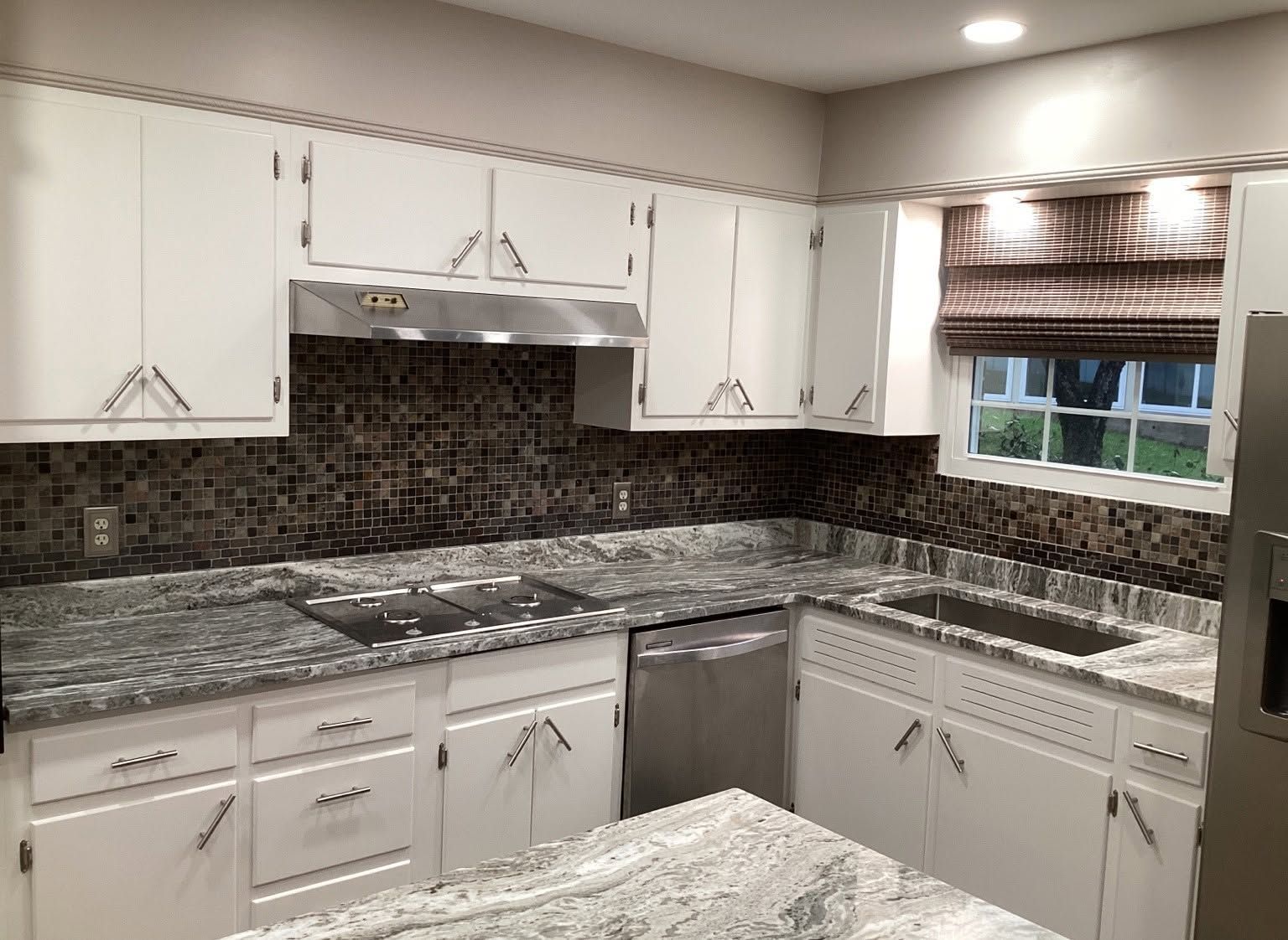Modern kitchen with white cabinets, dark mosaic backsplash, granite countertops, and stainless steel appliances