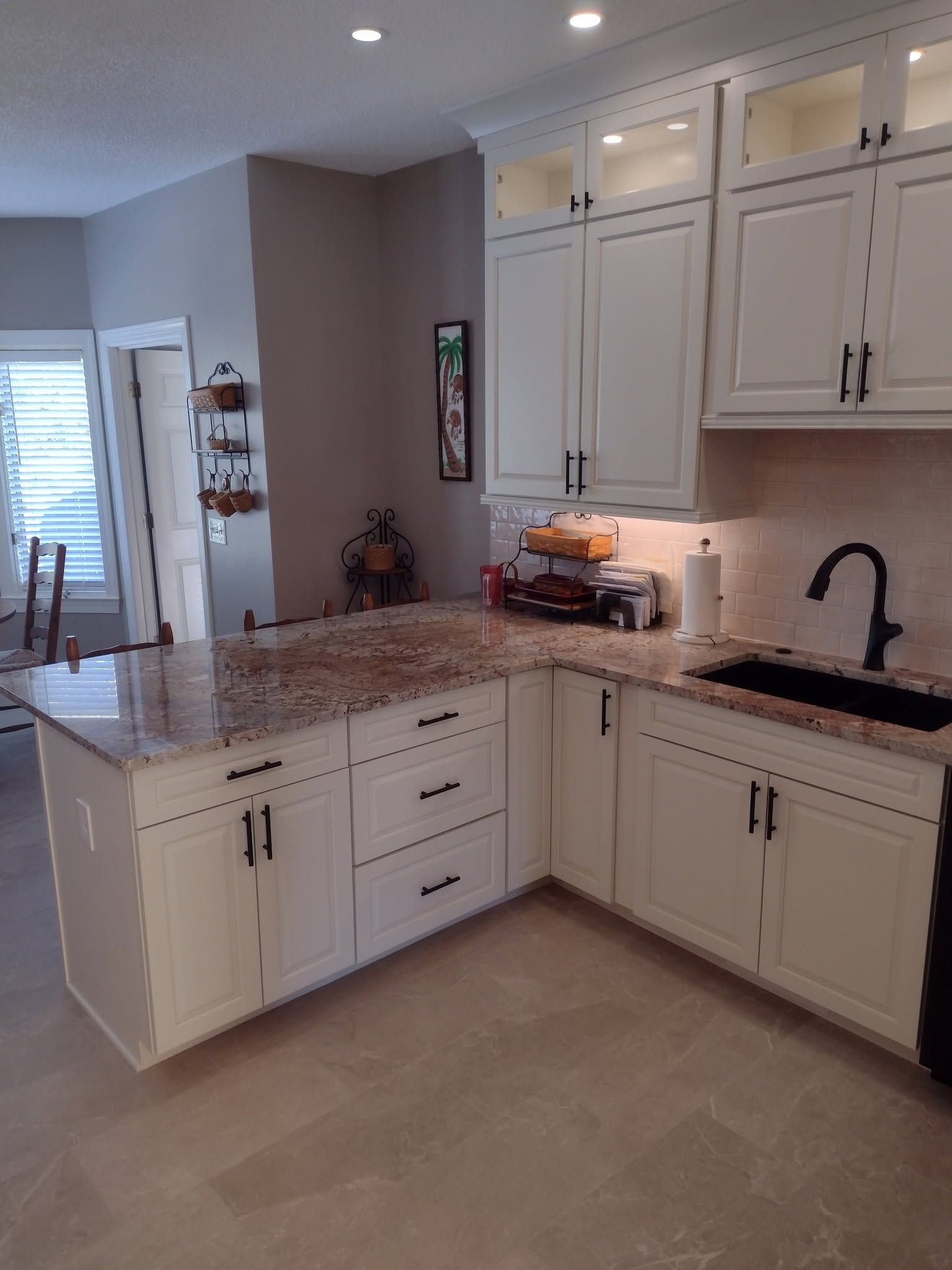 Bright kitchen with white cabinets, granite countertops, black faucet, and beige tile floor.