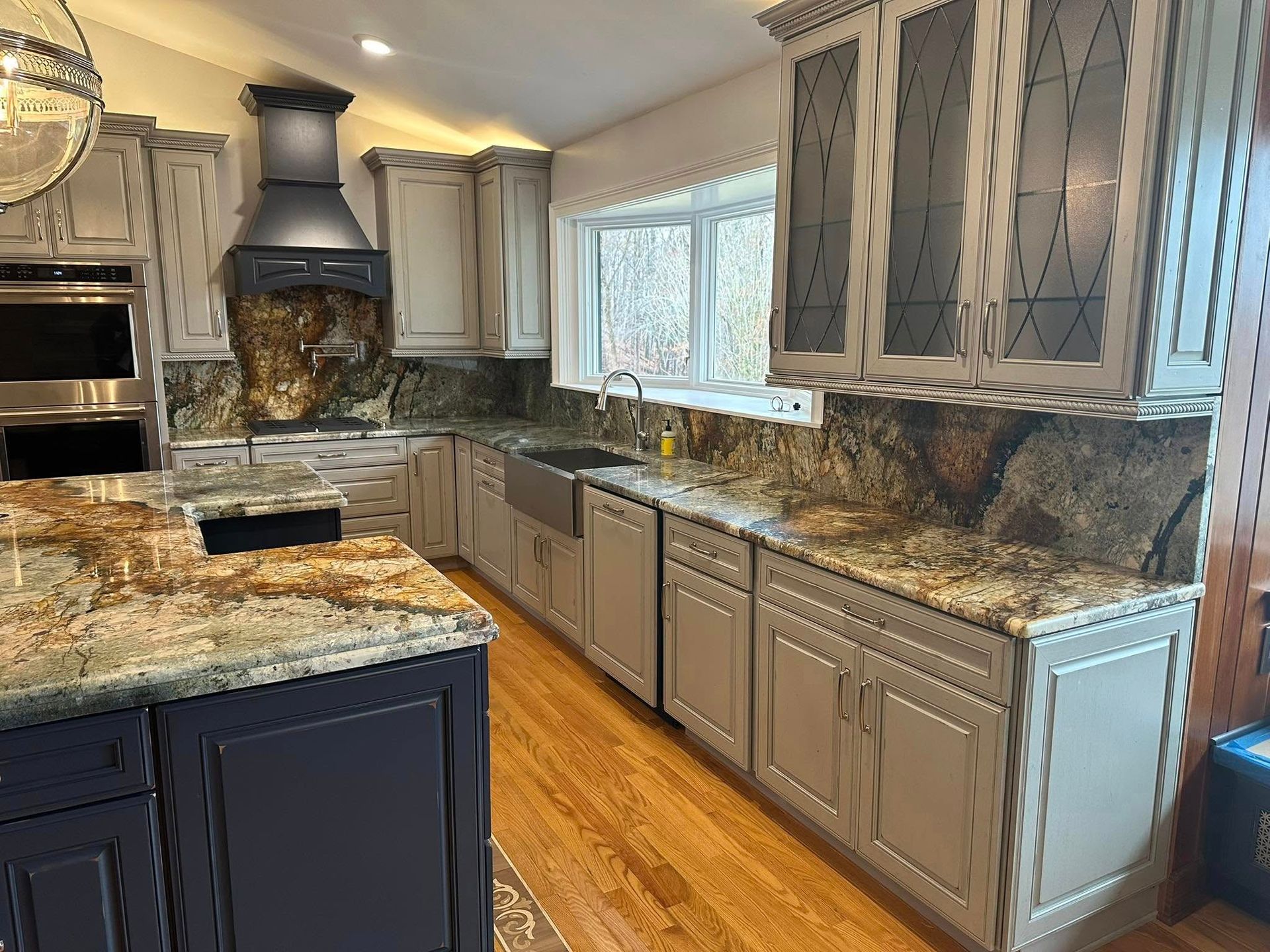 Modern kitchen with gray cabinets, granite countertops, stainless range hood, and hardwood floor