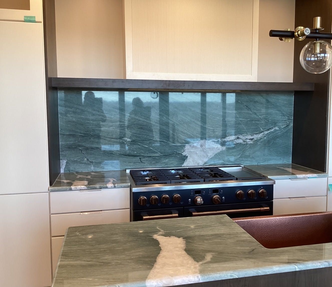Modern kitchen with a stovetop in front of a wide window and reflective backsplash.