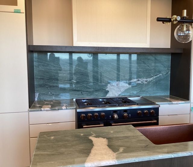 Modern kitchen with a stovetop in front of a wide window and reflective backsplash.