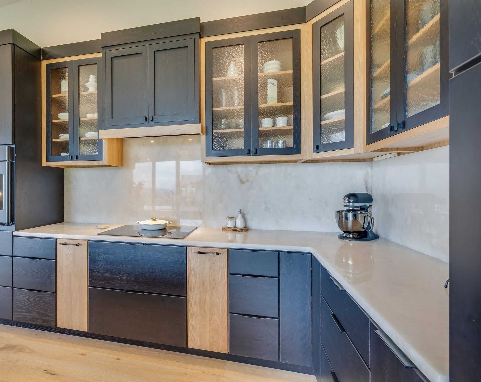 Modern kitchen with dark cabinets, white countertops, glass-front uppers, and a stand mixer on the counter