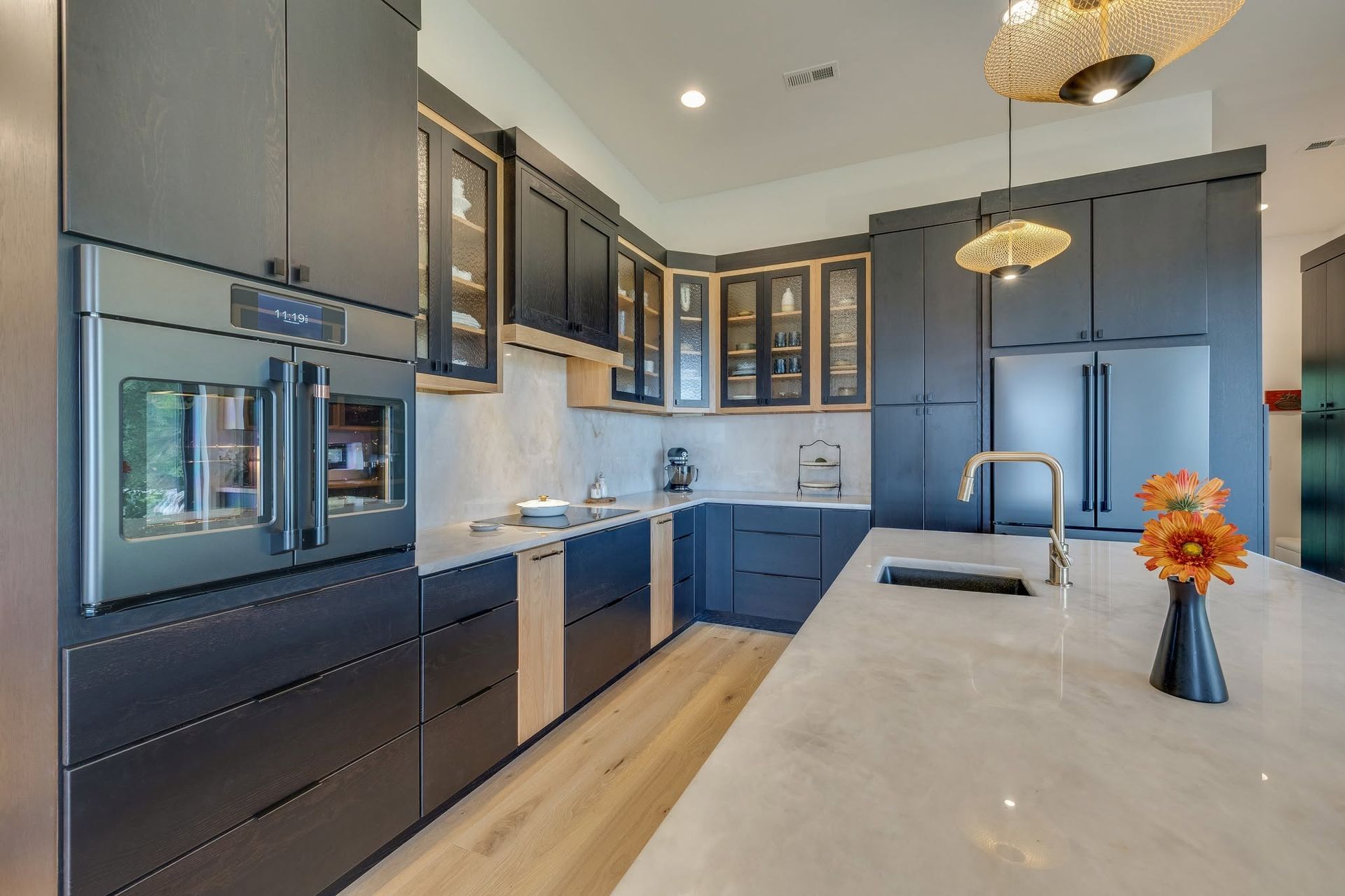 Modern kitchen with navy cabinets, large island, and stainless steel appliances, lit by pendant lights