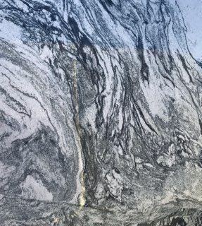 Aerial view of a rocky, gray-and-white mountain slope with dark streaks and a narrow valley below
