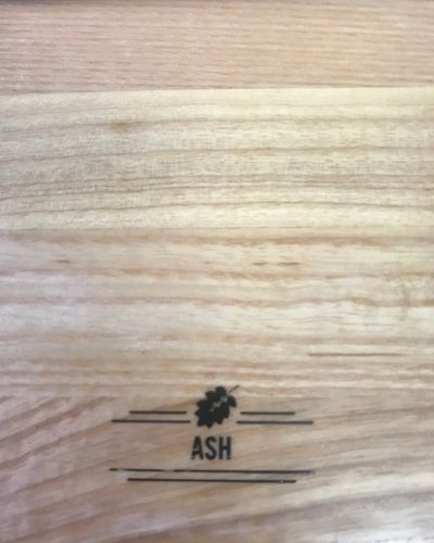 Wooden surface with a small black leaf logo and the word “ASH” printed near the center.